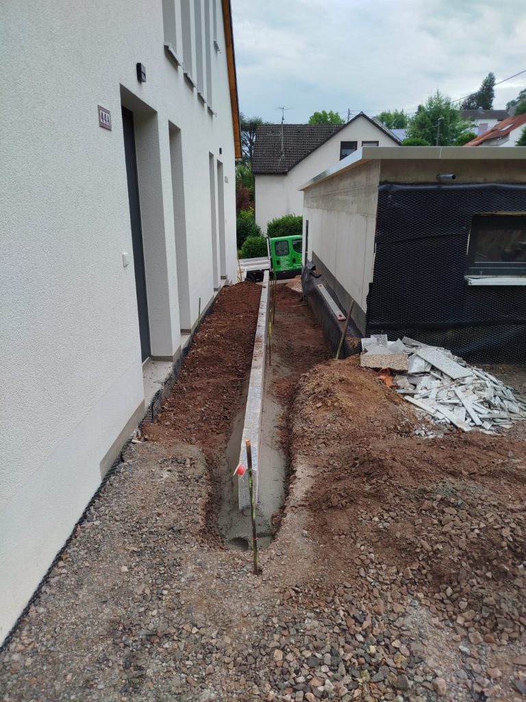 Ausgehobener Graben entlang einer Hauswand für Erd- und Pflasterarbeiten