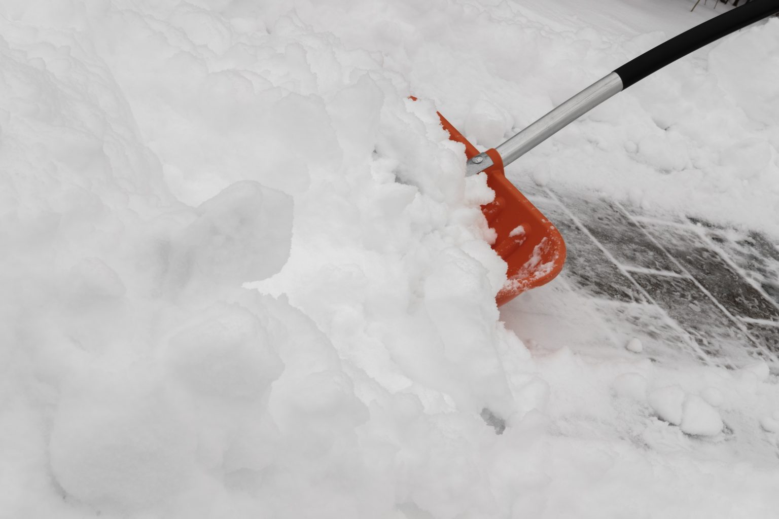 Schneeschaufel räumt Schnee von einem gepflasterten Weg